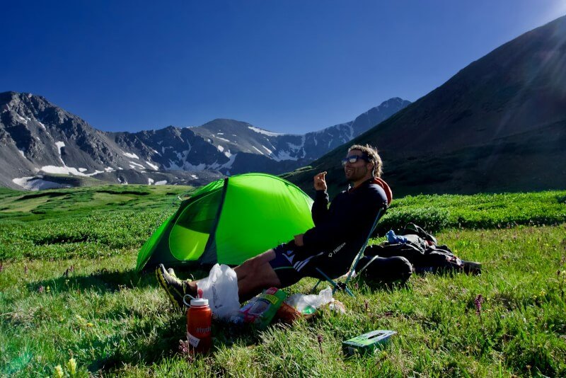 man sitting on black camping chair beside green dome tent